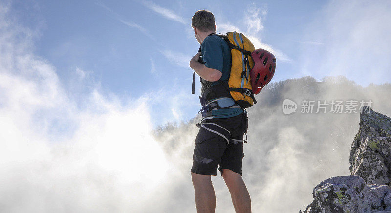 一名年轻人在一座via ferrata攀爬的山顶透过云层观看日出